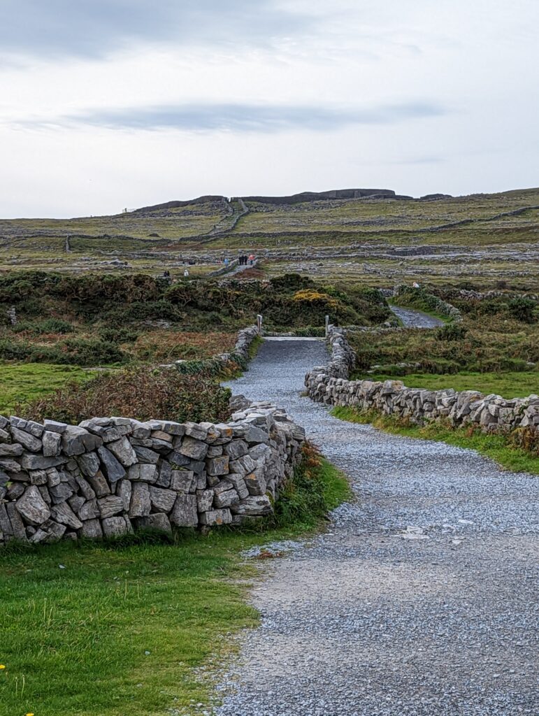 A road made of gravel with no hoses around and stone walls on both sides of the road