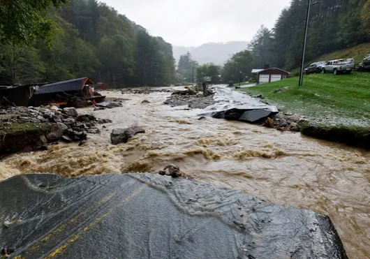 Flooded river with debris and a damaged road.