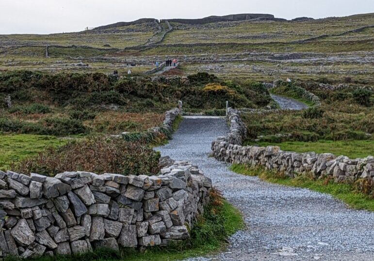 A road made of gravel with no hoses around and stone walls on both sides of the road